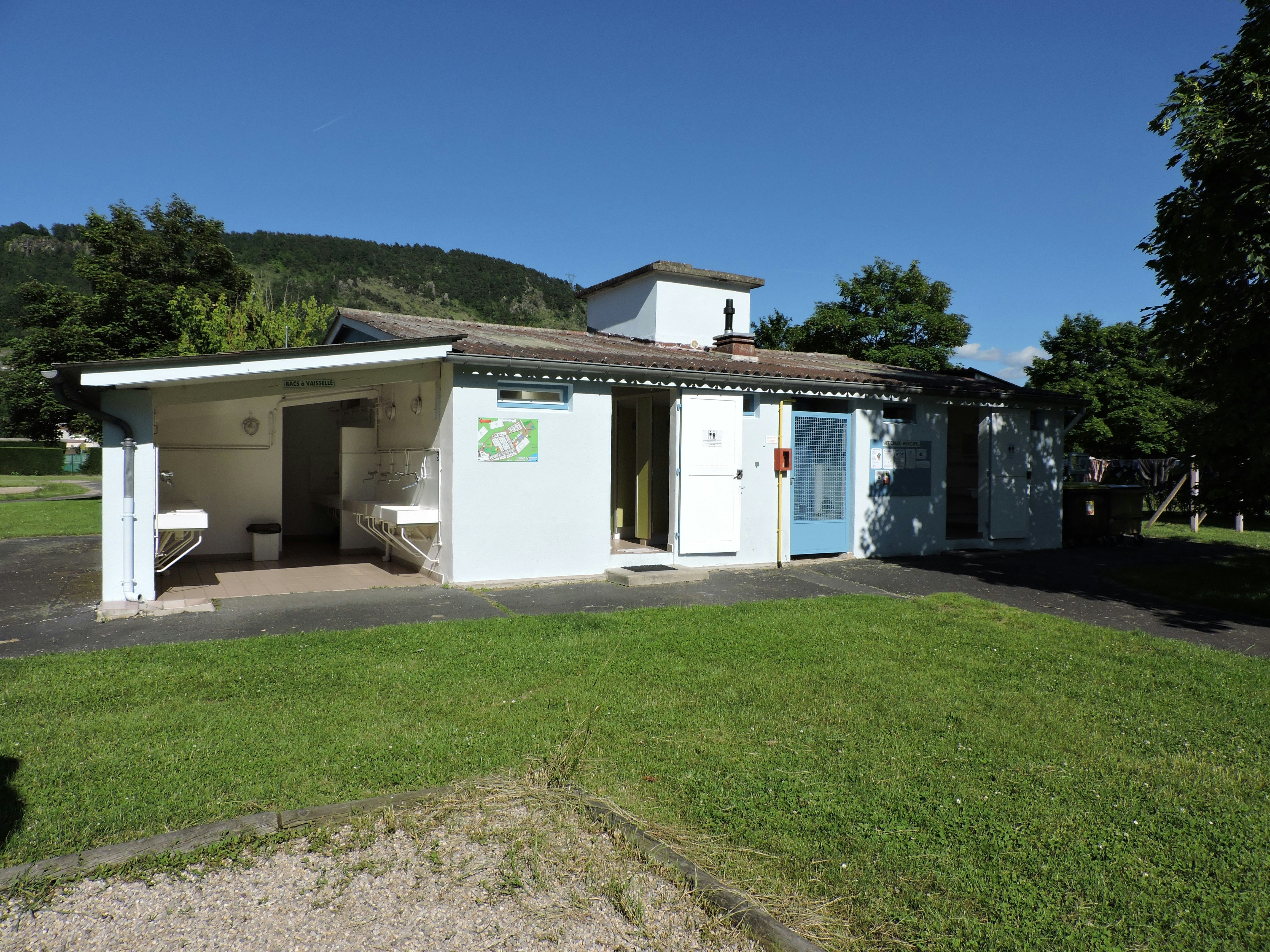 Wohnmobil-ähnliches Ferienhaus mit Terrasse, Markise und Rasenfläche im Campingbereich, im Hintergrund Bäume und Hügel.