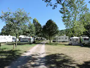Campingplatz mit Wohnwagen und Wohnmobilen auf Stellplätzen, dazwischen ein Weg und Bäume im Grünen.