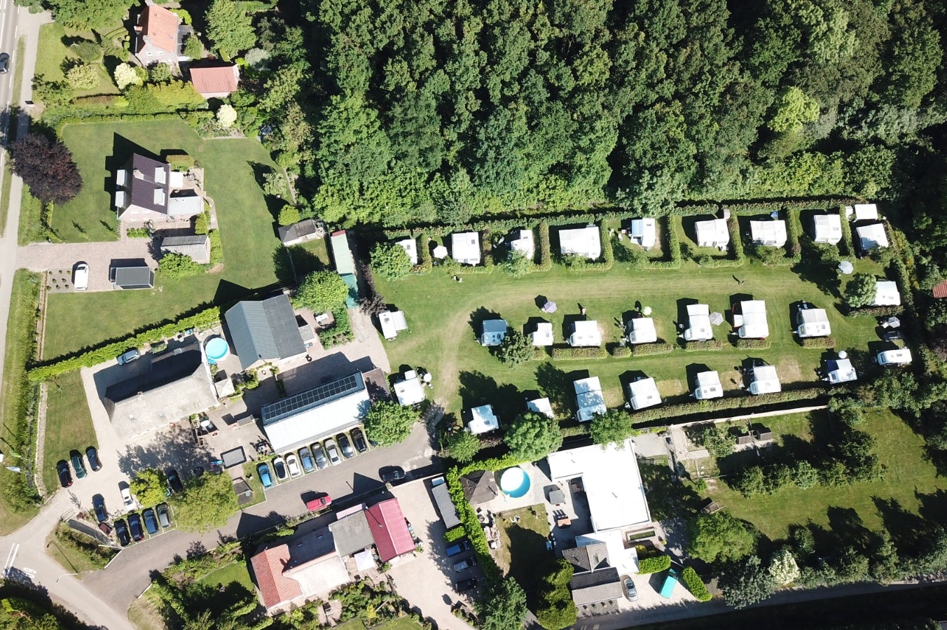 Luftaufnahme eines Campingplatzes mit Stellplätzen, Wohnmobilen und Zelten, umgeben von Bäumen und Wegen.