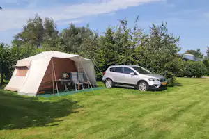 Zelt auf grünem Rasen mit Vorzelt, daneben ein Auto und Hecken sowie Bäume im Hintergrund.