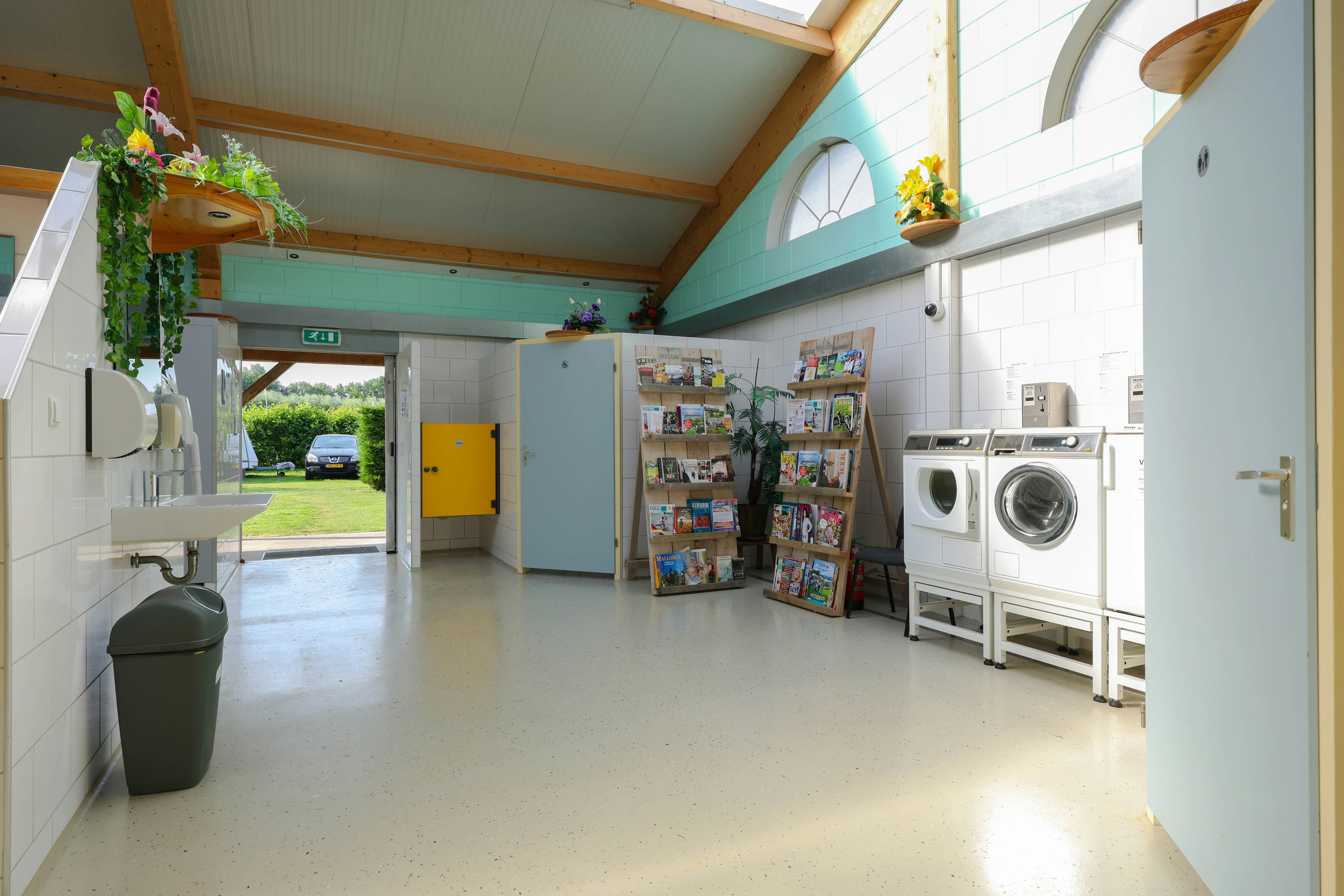 Innenraum eines Campinghauses mit Küchenzeile, Regalen und Waschmaschine, daneben ein Wäschekorb und große Fensterfront.