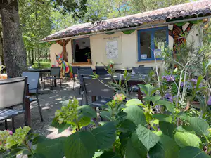 Campinghaus mit Terrasse, Gartenpflanzen und Sitzgruppe aus Stühlen und Tisch vor dem Eingang, umgeben von Bäumen.