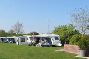 Campingplatz mit Wohnmobil und Vorzelt auf dem Rasen, daneben weitere Zelte und Wohnwagen, Bäume im Hintergrund.