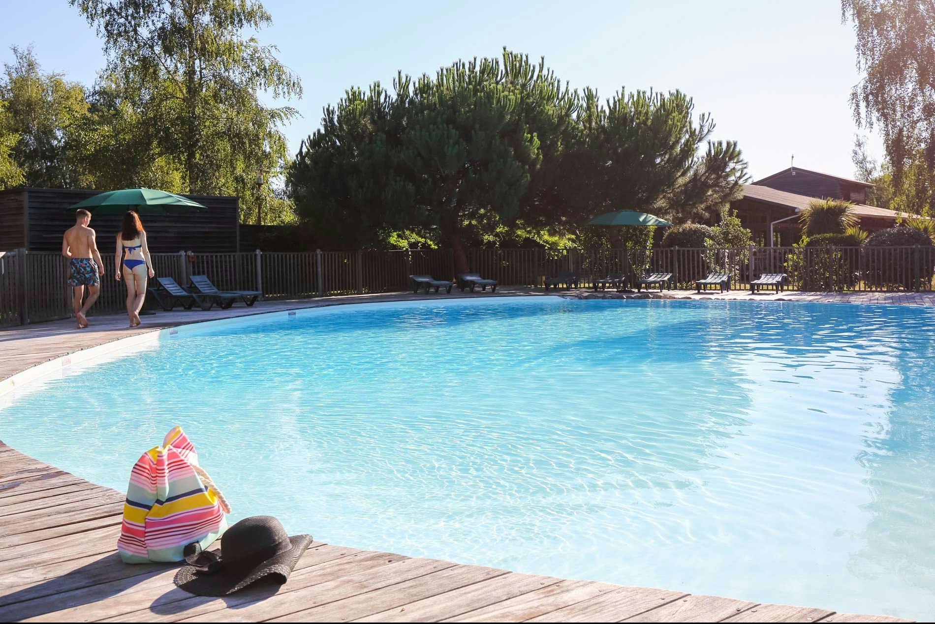 Großer Camping-Pool mit Holzsteg, Liegen und Zaun im Hintergrund, daneben ein buntes Spielzeug am Beckenrand.