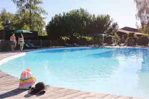 Großer Camping-Pool mit Holzsteg, Liegen und Zaun im Hintergrund, daneben ein buntes Spielzeug am Beckenrand.