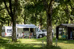 Campingplatz im Grünen: Wohnmobil mit Vorzelt, daneben Sitzgruppe und Tisch, im Hintergrund weitere Zelte zwischen Bäumen.