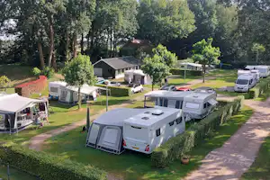 Campingplatz mit Wohnmobilen und Wohnwagen auf Stellplätzen, dazwischen Rasenwege und Bäume, im Hintergrund kleine Gebäude.