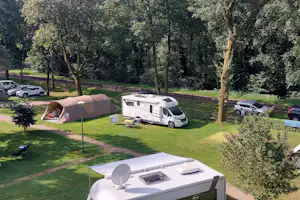 Wohnwagen und Zelte auf einem Campingplatz inmitten von Bäumen, mit Rasenflächen und Stellplätzen.