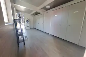 Heller Waschraum im Campinghaus mit weißen Schränken, Holzfußboden und einem kleinen Wagen mit Spendern am Eingang.
