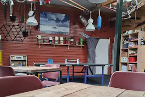 Camping-Lounge unter Zeltdecke mit Holztisch, Sitzgelegenheiten, Lampen und Deko-Figur an der Wand.