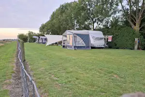 Campingzelt auf einer grünen Wiese, daneben weitere Zelte und Bäume am Rand des Campingplatzes.