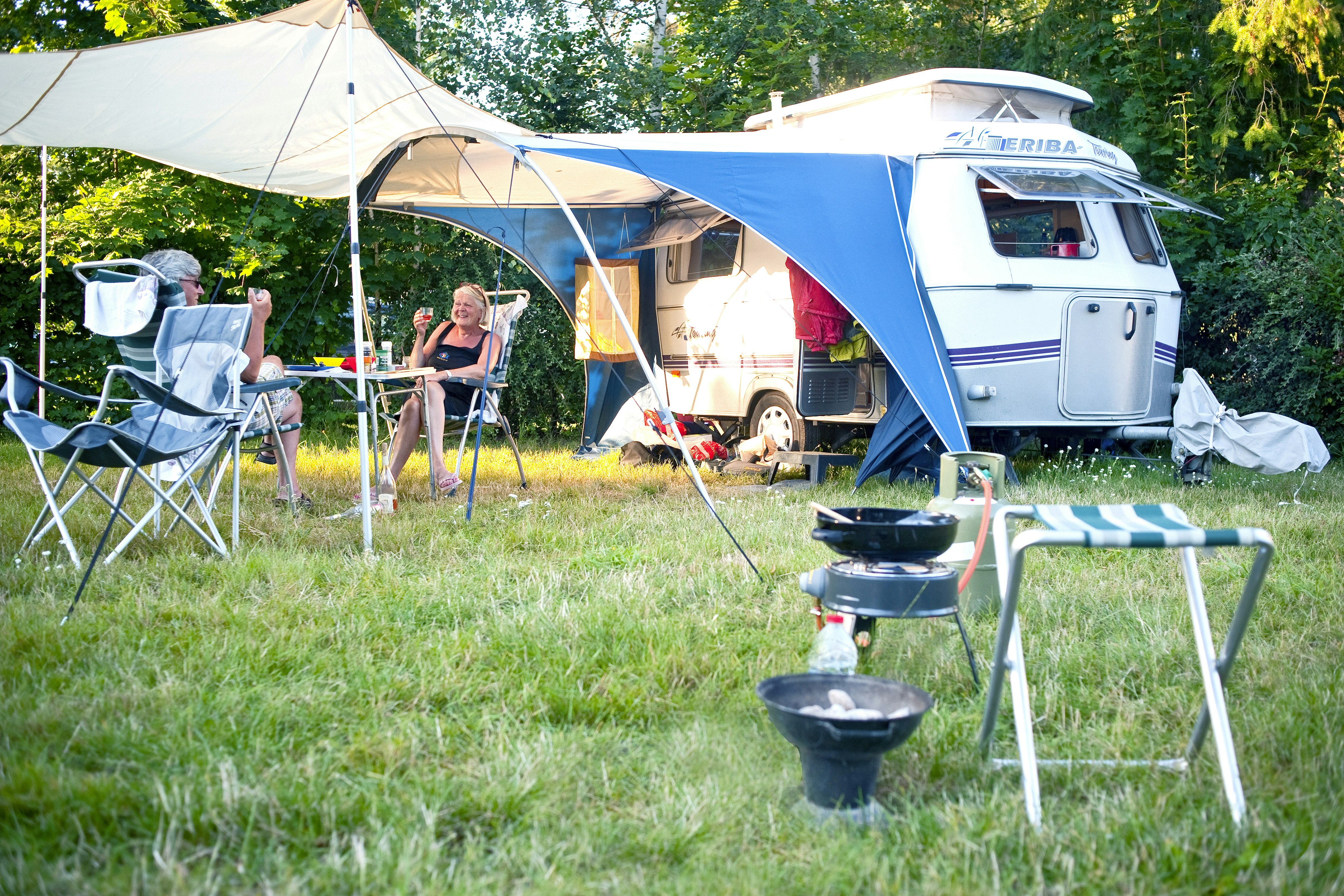 Camping De Bron - Camper sitzen vor dem Wohnmobil im Schatten der Markise