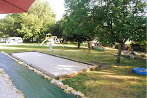 Spielbereich auf dem Campingplatz: Rasen, Sandkasten und Rutsche neben einem großen Zelt unter Bäumen.
