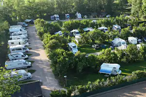 Luftaufnahme eines Campingplatzes mit Wohnwagen und Zelten, gepflasterten Wegen, Hecken und Bäumen im grünen Umfeld.