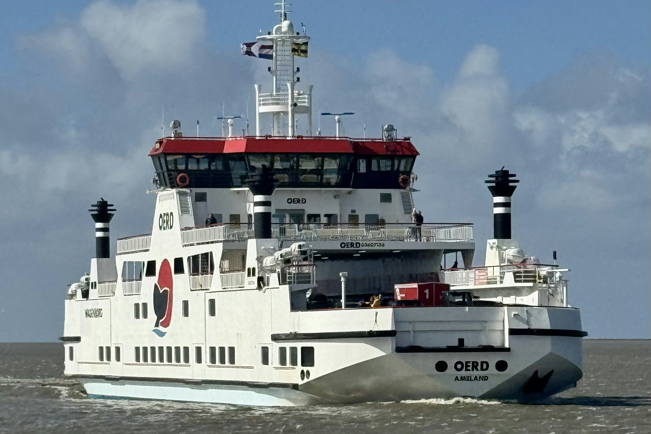 Frachtschiff auf dem Wasser, weißes Schiff mit rotem Streifen und Brücke, Schornsteine und Deckaufbauten vor blauem Himmel.