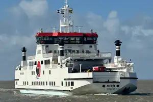 Frachtschiff auf dem Wasser, weißes Schiff mit rotem Streifen und Brücke, Schornsteine und Deckaufbauten vor blauem Himmel.