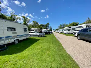 Wohnmobile und Autos auf einem Campingplatz-Stellplatz, mit Kiesweg zwischen den Parzellen und gepflegtem Rasen.