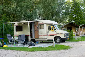 Wohnmobil am Stellplatz mit Vorzelt, Stühlen und Tisch auf dem Gras, im Hintergrund Bäume und weitere Campingunterkünfte.