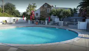 Rundes Camping-Pool mit blauem Wasser, Betonrand und weißen Zäunen; im Hintergrund ein Haus mit Terrasse und Bäumen.