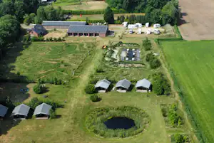 Luftaufnahme eines Campingplatzes mit mehreren Zelten, einem kleinen Teich, Wegen und umgebenden Wiesen und Bäumen.