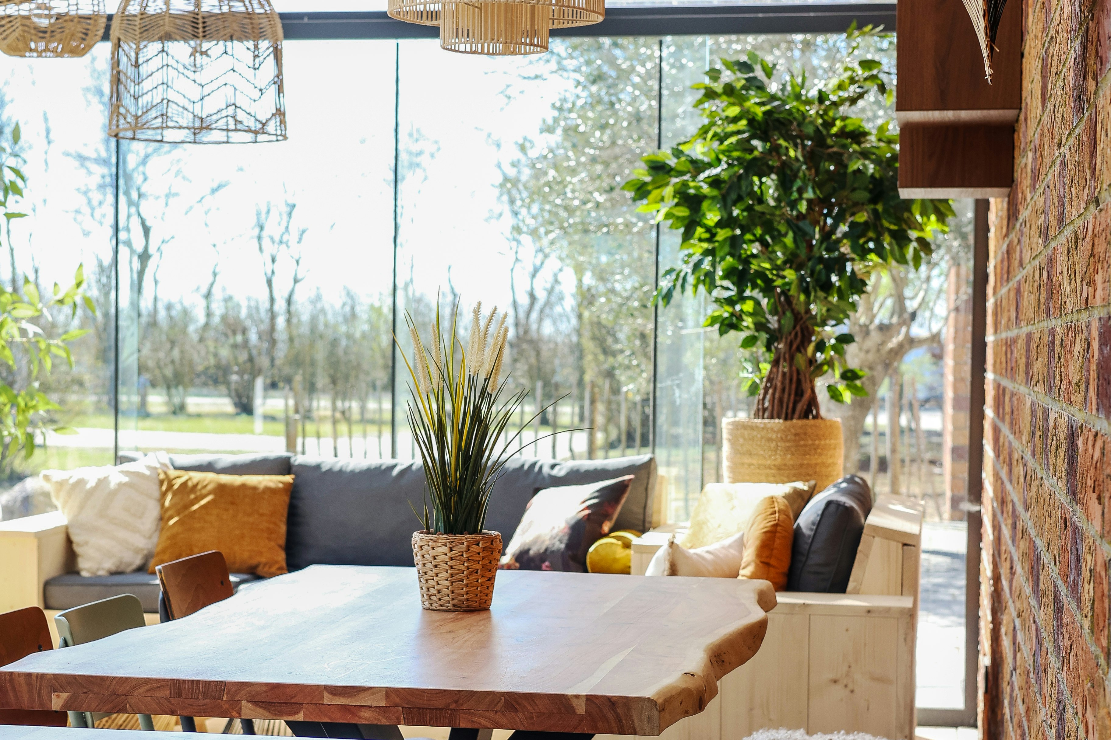 Überdachte Terrasse mit Holztisch und Sitzkissen, hängenden Lampen und Blick ins Grüne durch große Glasfronten.