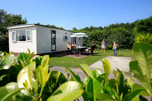 Camping De Holterberg - Gäste sitzen vor dem Mobilheim im Schatten der Bäume auf dem Campingplatz