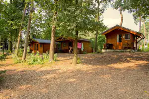 Holzhütten auf einem Campingplatz im Wald, mit Terrasse, Sitzbank und Wegen zwischen den Bäumen.