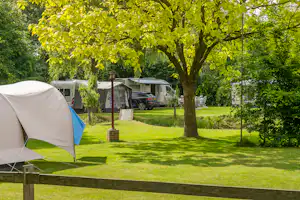 Zelt auf einem Campingplatz mit gepflegtem Rasen, daneben Wohnwagen und ein Auto, im Hintergrund Bäume und Hecken.