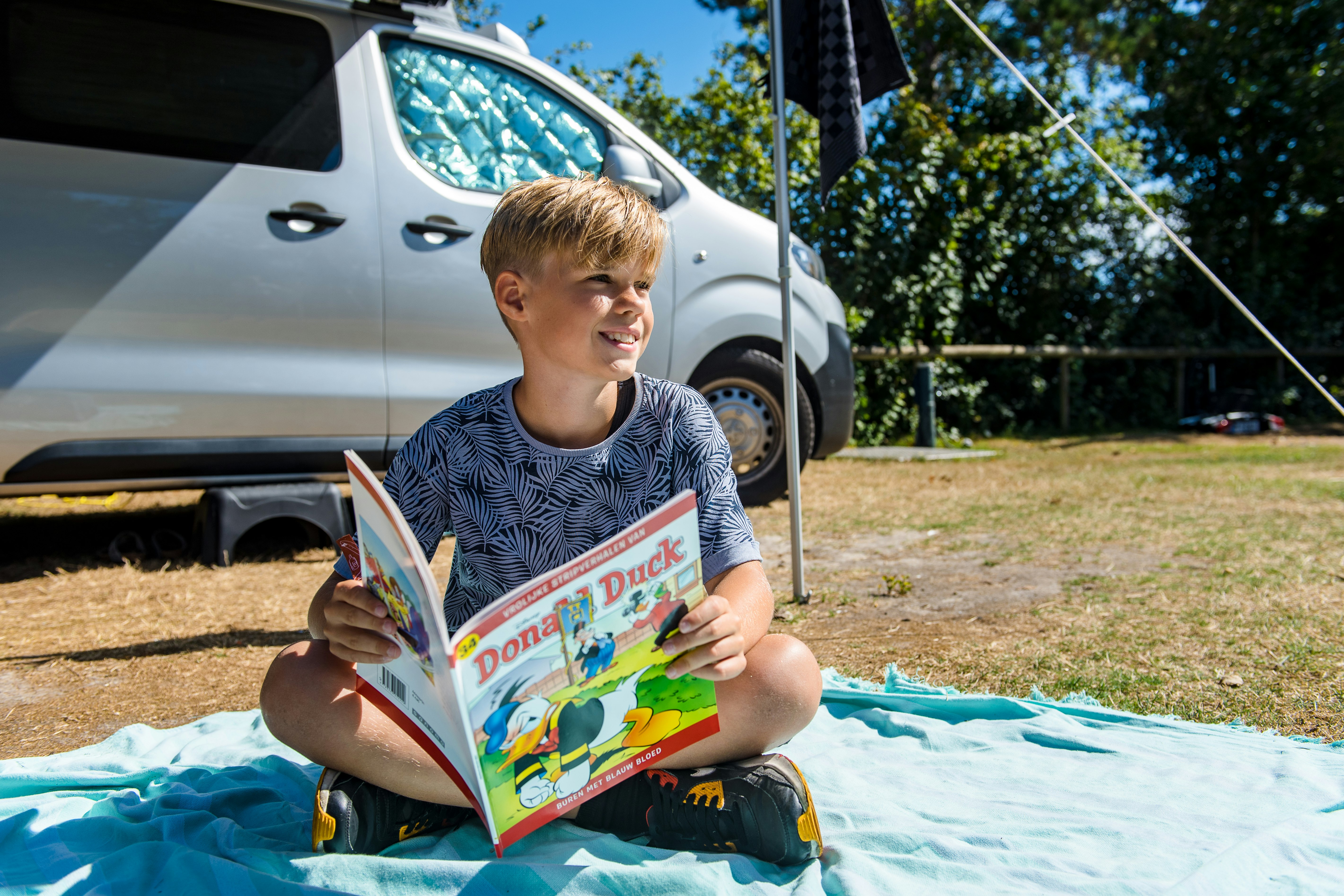 Camping De Kiekduun - Kind sitzt vor einem Standplatz und liest eine Zeitschrift
