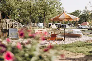 Großes Zelt mit Lichtergirlanden, daneben Wohnwagen und Campingfahrzeuge auf einem Stellplatz im Grünen.