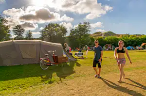 Zelt auf einem Campingplatz, daneben ein Fahrrad und Liegestühle; im Hintergrund weitere Zelte und Personen auf dem Rasen.