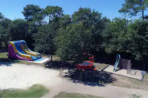 Spielplatz mit Rutsche und Sandfläche, daneben ein aufblasbares Hüpf- und Rutschgerät auf dem Campingplatz im Grünen.