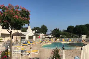 Camping-Pool mit blauen und gelben Liegen, Sonnenschirmen und weißen Zelten hinter einem Zaun, im Hintergrund Bäume.
