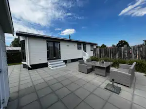 Mobilheim mit Terrasse aus Fliesen, Sitzgruppe und Sichtschutzzaun, daneben Eingang und Fenster an der Hauswand.