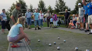 Boule-Spiel auf dem Campingplatz: mehrere Personen stehen am Rand, daneben ein Golfwagen und ein paar Kinder auf dem Rasen.