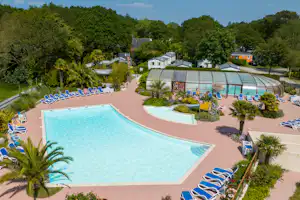 Großer Camping-Pool mit türkisfarbenem Wasser, Liegen und gepflegten Beeten, im Hintergrund Bungalows und Bäume.
