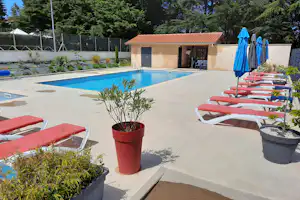 Schwimmbad auf der Camping-Terrasse mit roten Liegen, Töpfen und Blick auf das kleine Gebäude und Bäume.