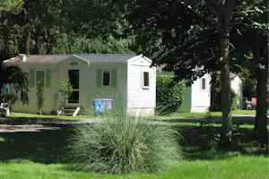 Mobilheim mit grünen Türen und Fenstern, Rasen und Bäumen im Hintergrund auf dem Campingplatz.