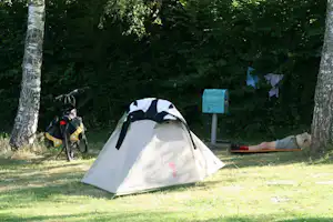 Zelt auf einem grasigen Campingplatz zwischen Bäumen, daneben ein Fahrrad und ein Schild am Wegesrand.