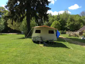 Wohnwagen auf einem grünen Campingplatz auf einer Wiese, mit Vorzelt und Leinen, umgeben von Bäumen und Hecken.