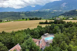 Blick von oben auf Campinganlage mit Pool, umgeben von Bäumen, Feldern und Bergen im weiten Tal.