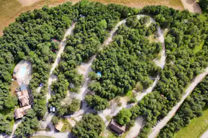 Luftaufnahme einer Campinganlage mit Pool, Wegen und mehreren Stellplätzen zwischen dichtem Baumbestand.