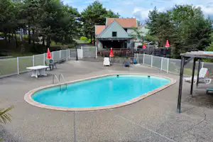 Campingpool auf der Terrasse mit Umzäunung, Liegestühlen und Tisch vor einem Holzhaus im Grünen.