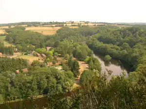 Blick auf einen Fluss durch Wald und Wiesen, mit Campingplatz-Gelände und kleinen Häusern im Tal.