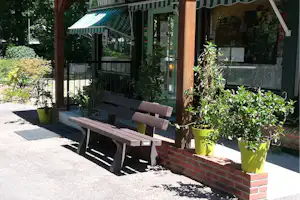 Terrasse am Camping-Eingang mit Bank, Sonnenschirm und vielen Topfpflanzen vor dem Gebäude.