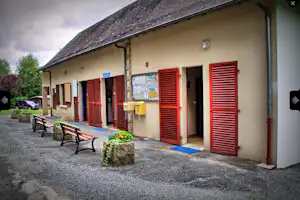 Campinggebäude mit roten Fensterläden, Sitzbank und kleinem Terrassenbereich vor dem Eingang, Kiesweg und Briefkasten.