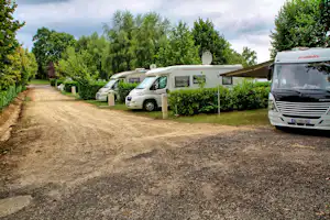 Wohnmobil auf dem Stellplatz am Campingplatz, daneben weitere Camper und Hecken, Kiesweg und Bäume im Hintergrund.
