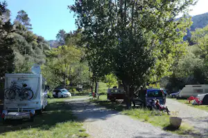 Wohnmobil-Stellplatz im Grünen mit geparkten Autos, Bäumen und Blick auf ein felsiges Tal im Hintergrund.
