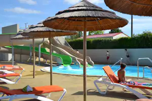 Camping-Pool mit blauem Wasser, Sonnenliegen und Sonnenschirmen, im Hintergrund Zelte und ein Zaun.
