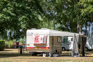 Wohnmobil mit Vorzelt und Campingstühlen am Stellplatz im Grünen, umgeben von Bäumen und einem kleinen Tisch.